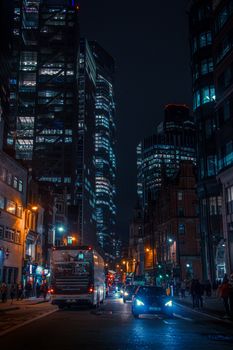 Bustling city street in London at night, featuring modern skyscrapers and busy traffic.