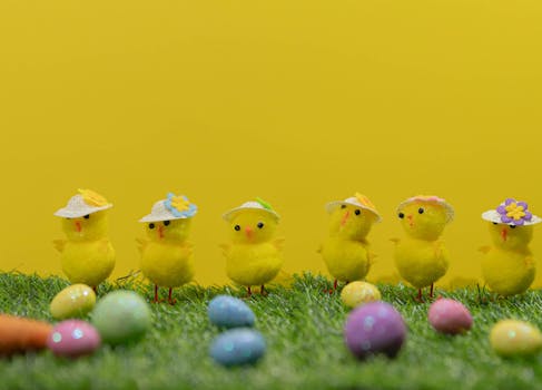 Colorful Easter setup with decorative chicks wearing hats and colorful eggs on grass.