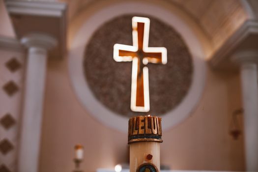 A glowing cross above an 'Alleluia' candle in a church, symbolizing faith and worship.