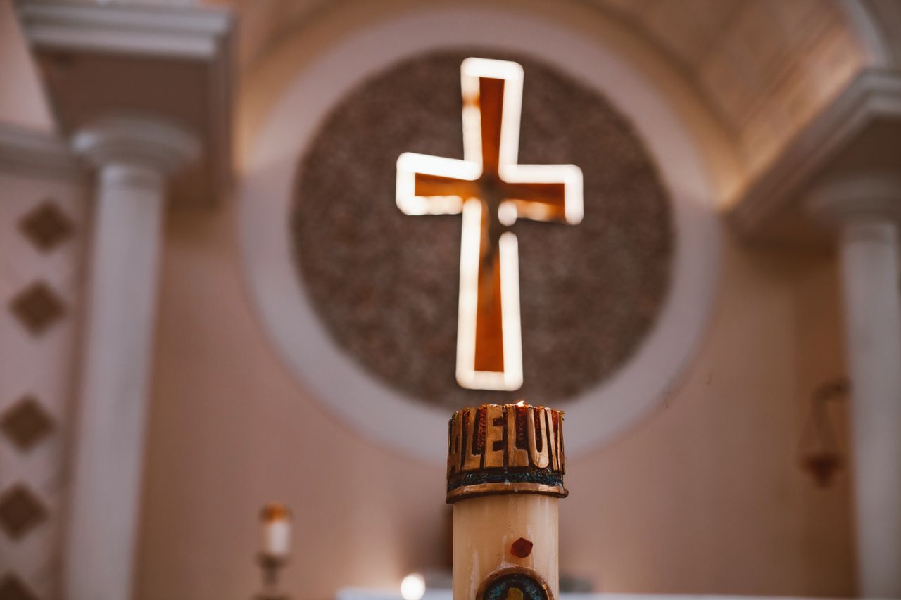 a glowing cross above an alleluia candle in a church symbolizing faith
