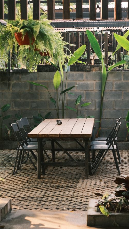 Free Tranquil outdoor patio featuring a rustic wooden table, chairs, and lush green plants. Stock Photo