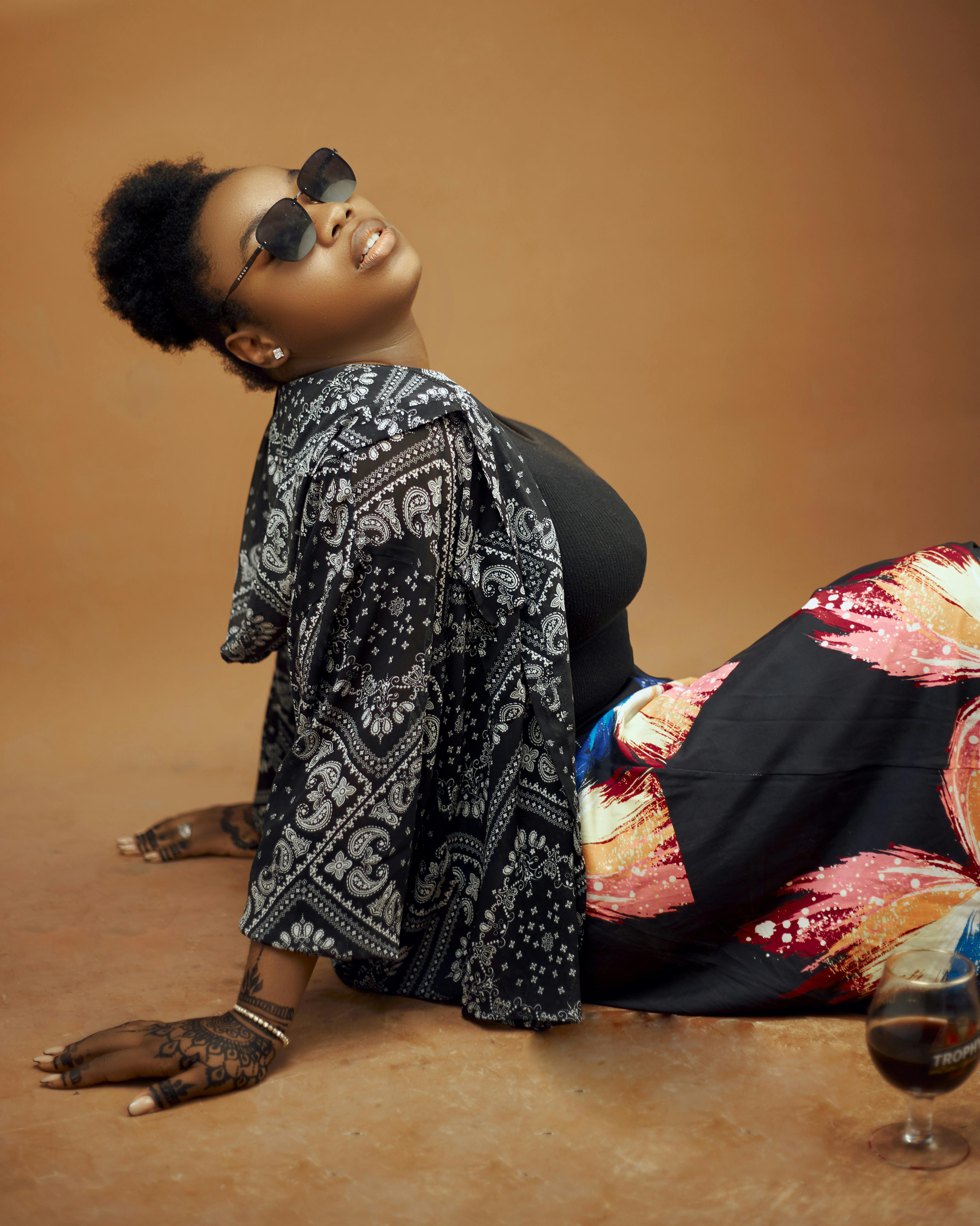 Stylish woman in sunglasses and printed attire posing elegantly indoors with henna designs.