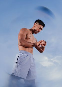 Muscular man outdoors checking his fitness tracker against a blue sky in San Martín, Perú.