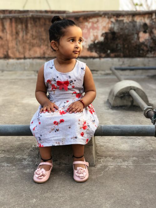 Free Adorable toddler girl in a floral dress sitting outdoors, looking thoughtful. Stock Photo