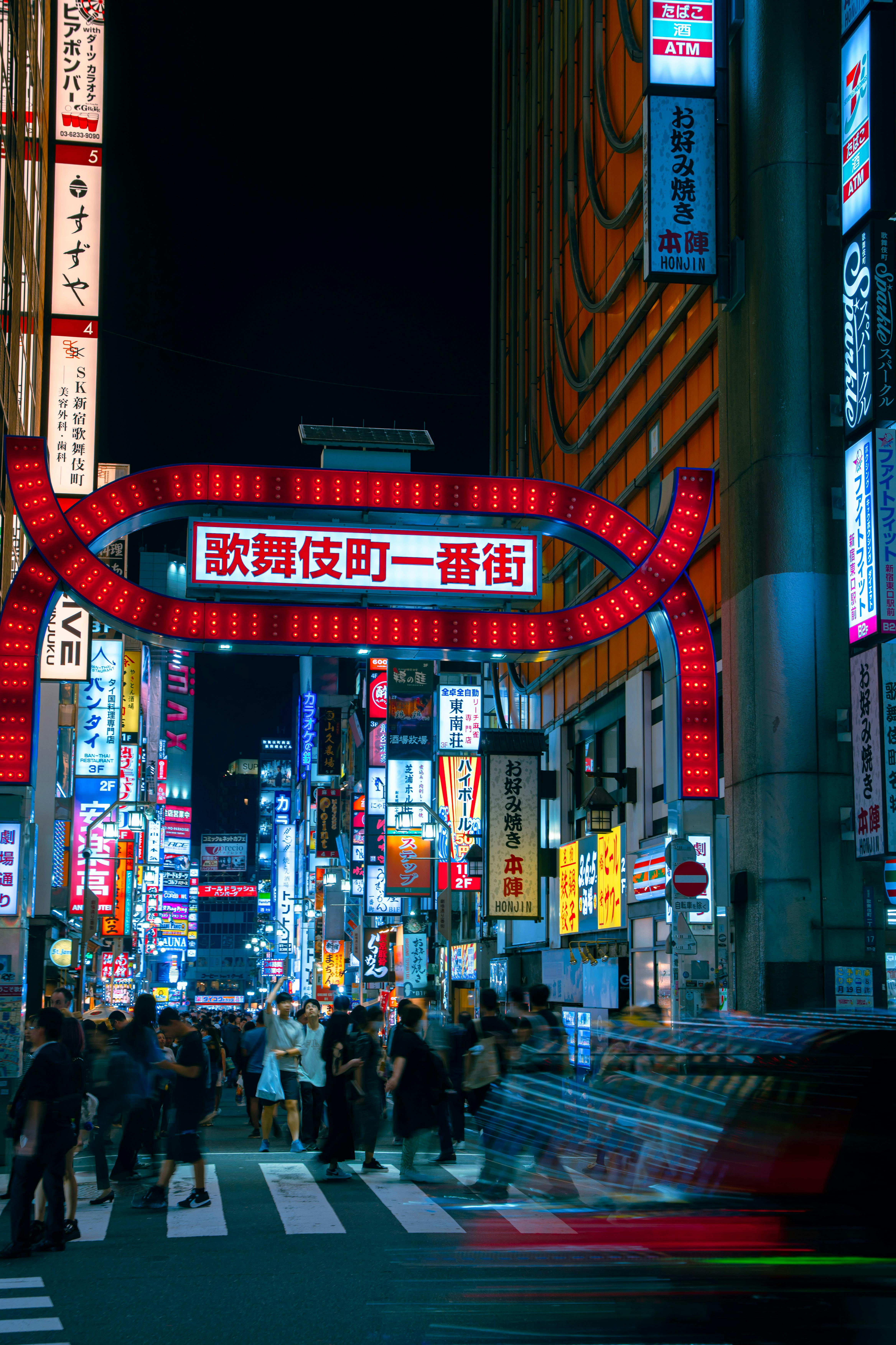 Dynamic street scene in Shinjuku, Tokyo at night, showcasing iconic Kabukicho signage and bustling city life.