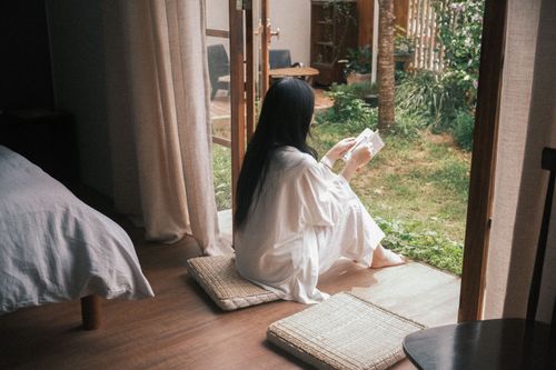 Free A woman reads a book by an open door, enjoying the garden view. Stock Photo