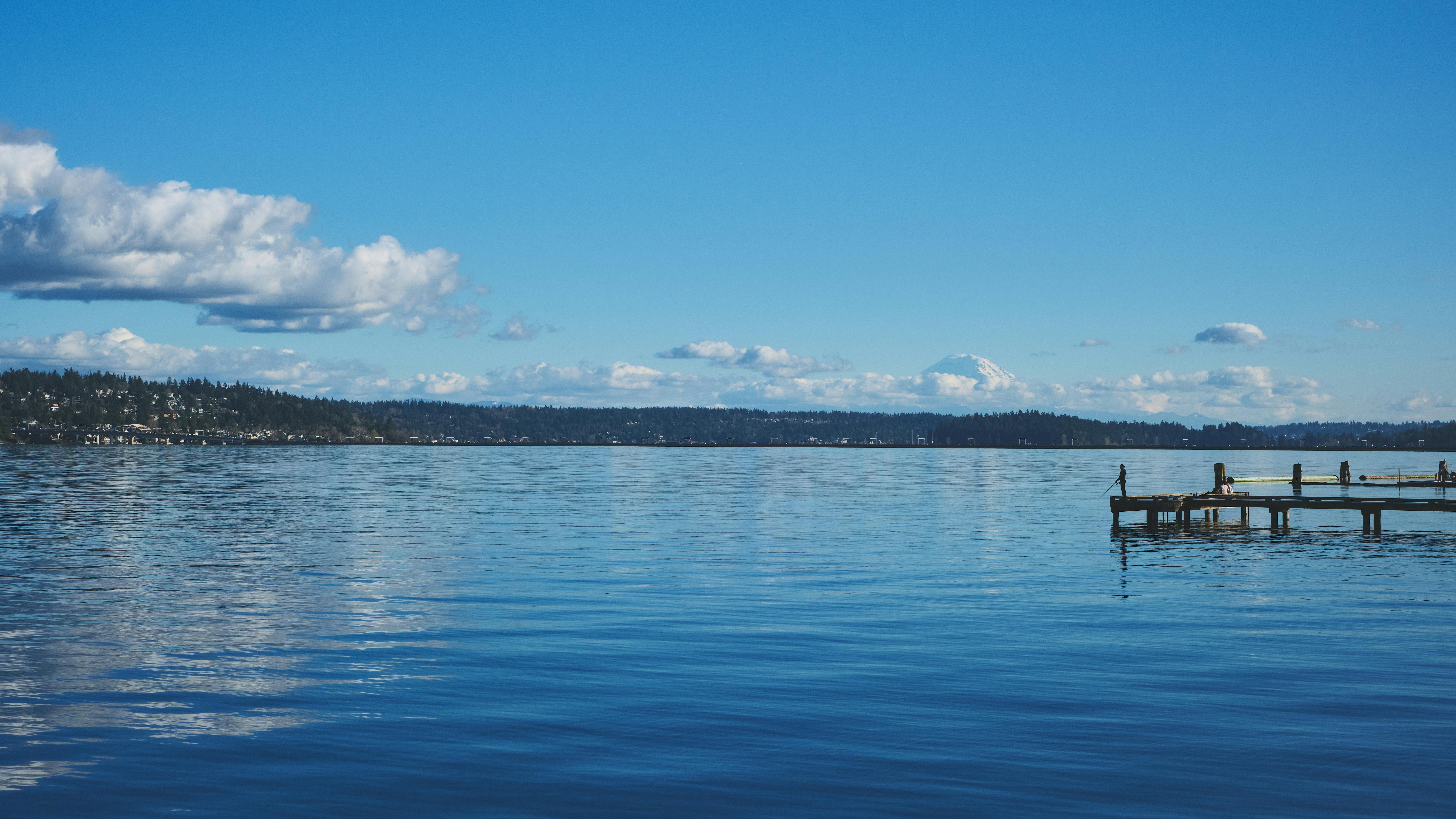 Serene lake scene with a pier and distant mountaintops under a clear blue sky in Washington.