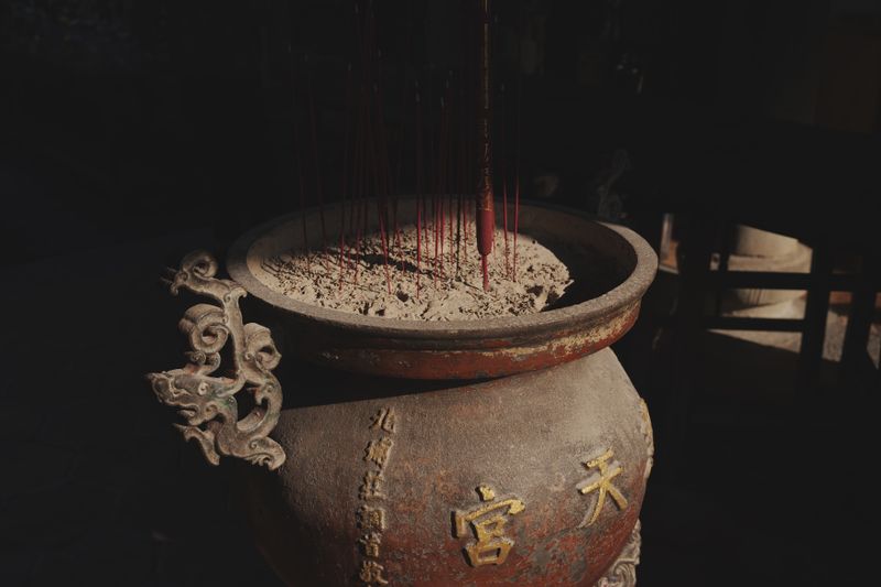 An ornate incense burner with ashes and sticks in a dimly lit temple, evoking spirituality.