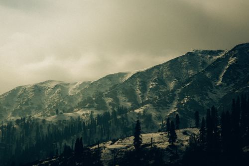 Free Moody and dramatic view of snow-covered mountains under a cloudy sky, ideal for winter-themed projects. Stock Photo