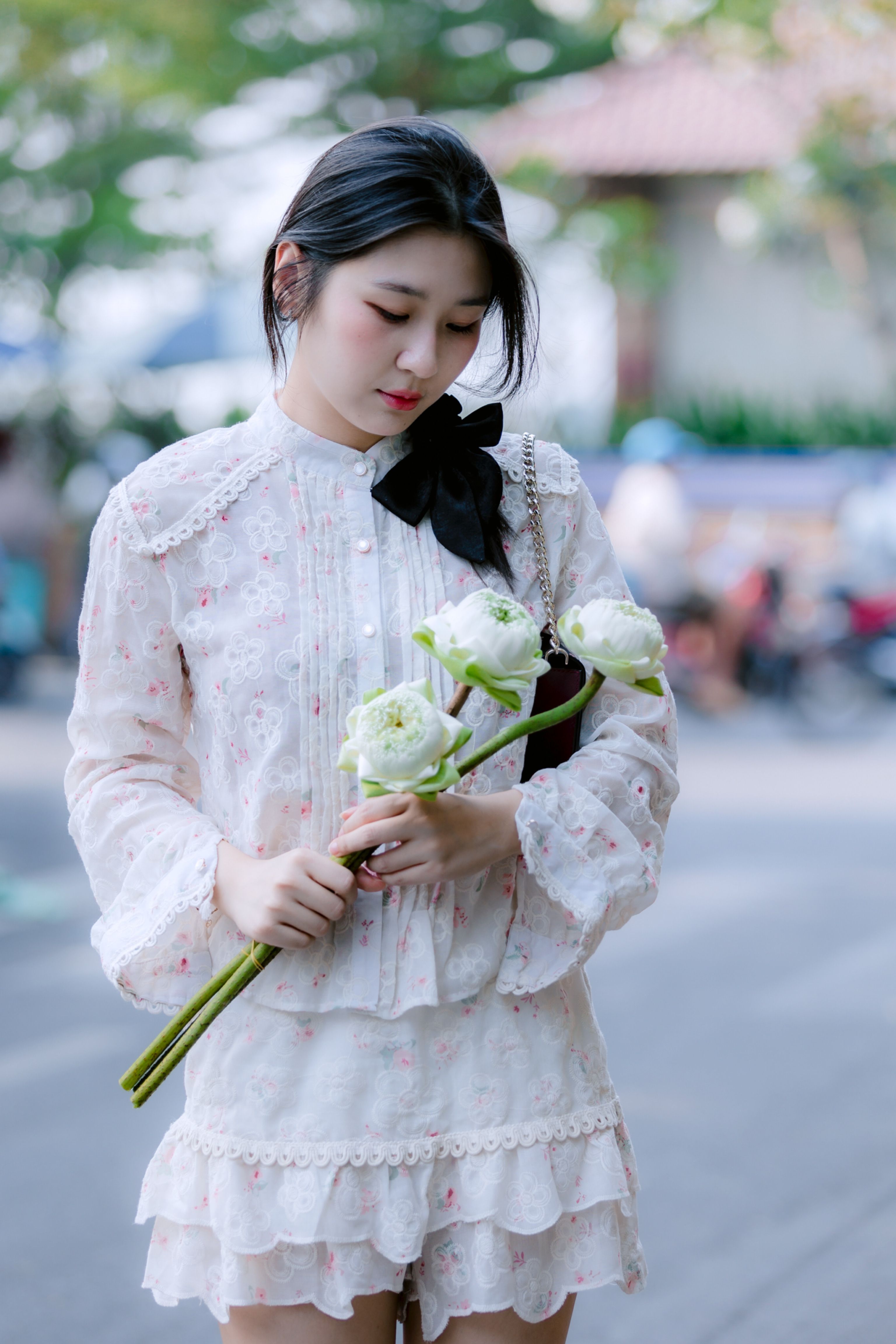 Young woman holding white flowers in a delicate dress outdoors.