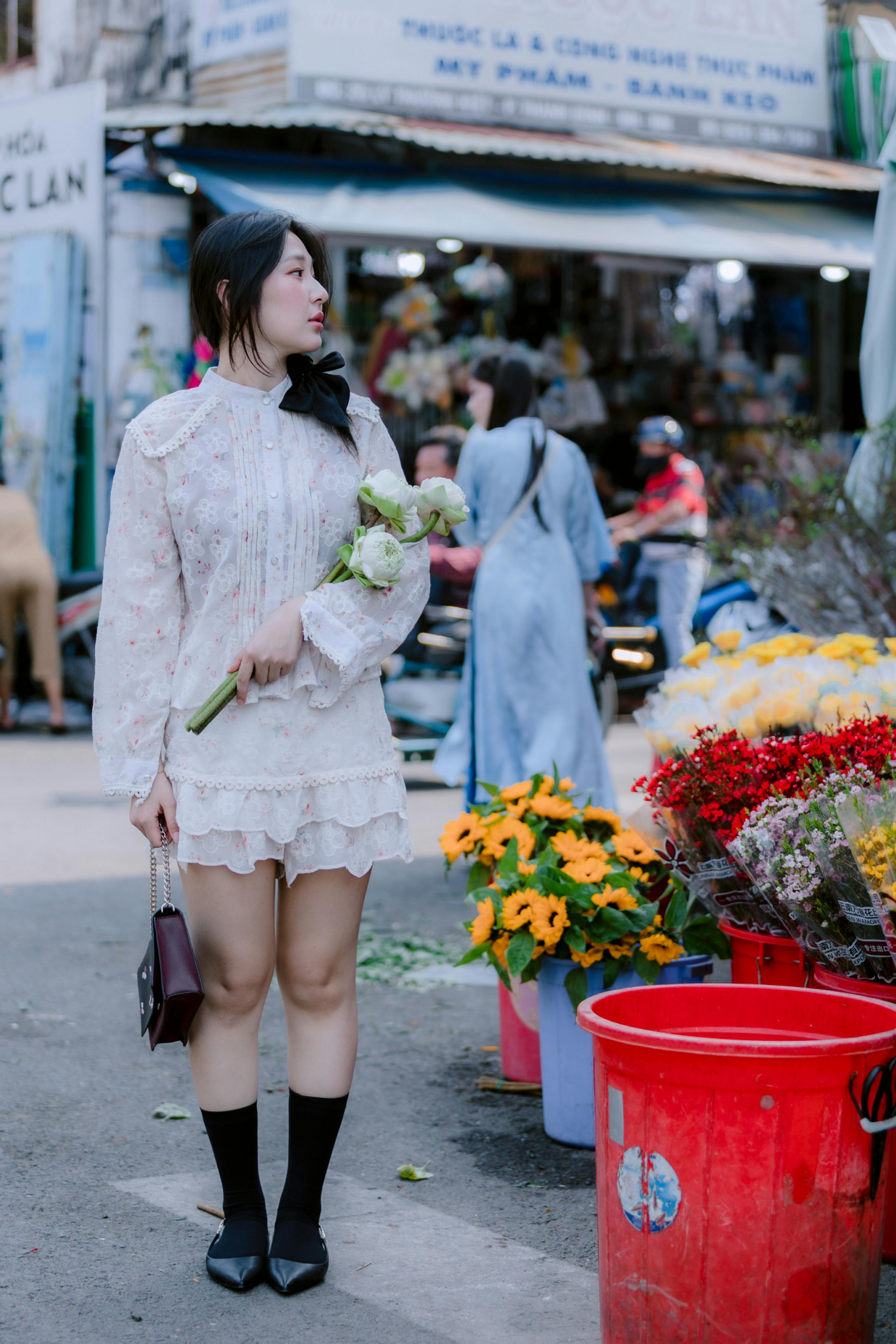 Woman holding flowers in a colorful outdoor market, surrounded by vibrant blooms.