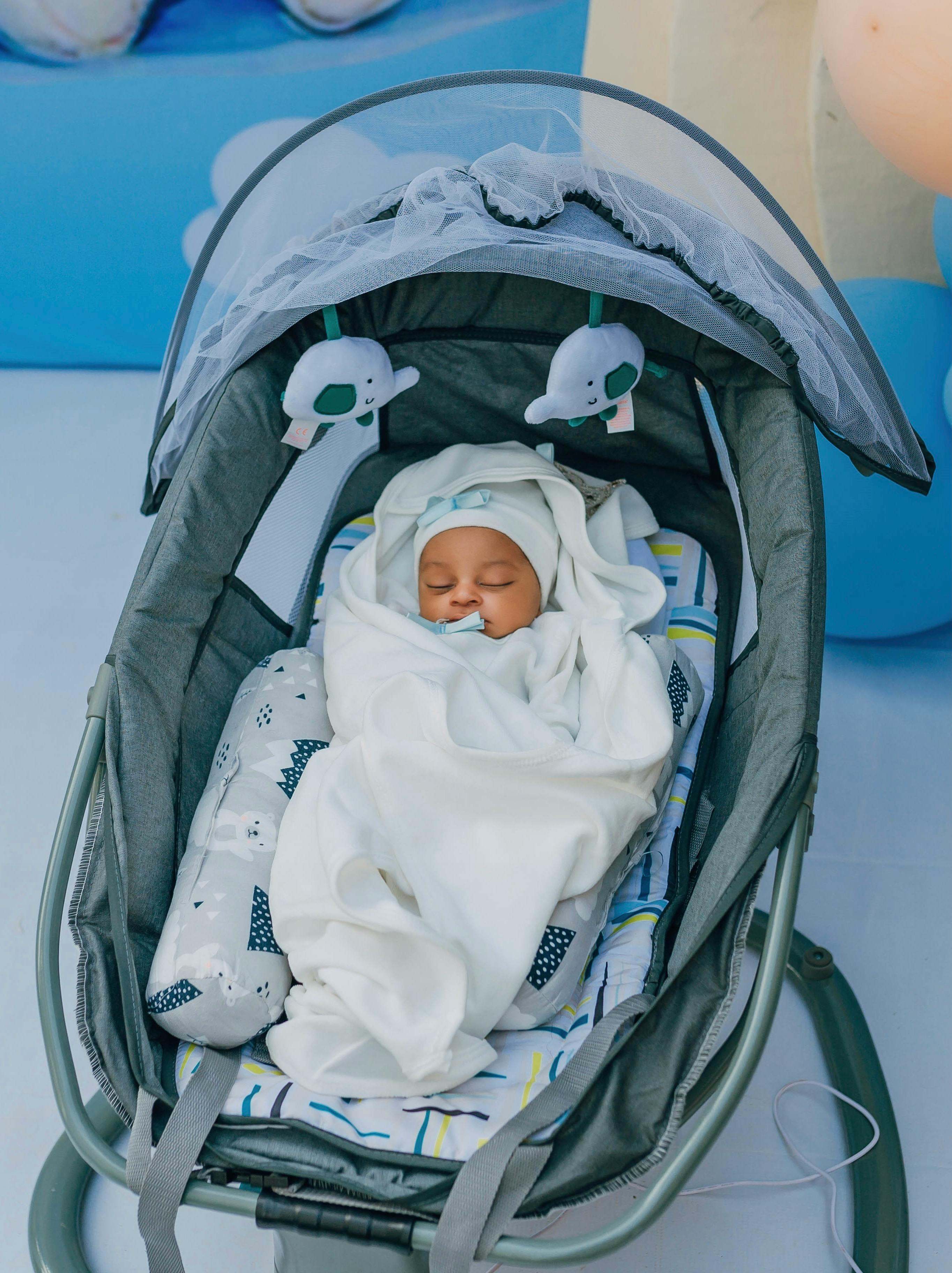 A serene baby sleeping peacefully in a comfortable stroller wrapped in a white blanket.