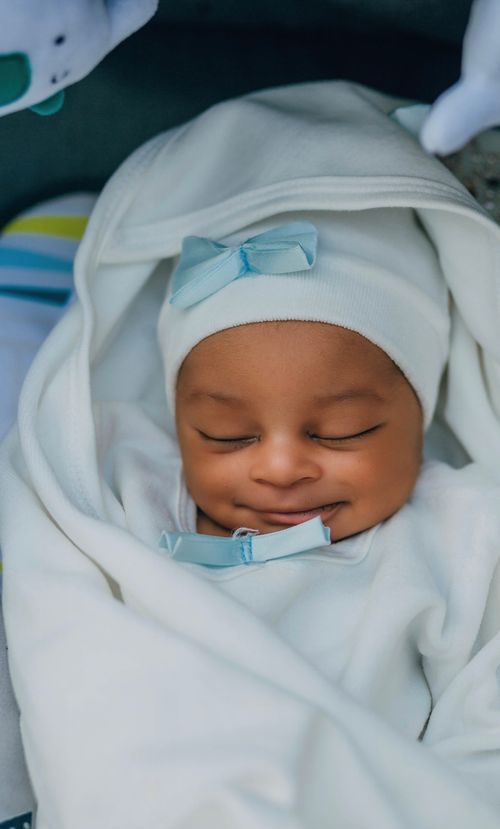 Free Adorable baby peacefully sleeping with a blue bow accent, wrapped in a cozy white blanket. Stock Photo