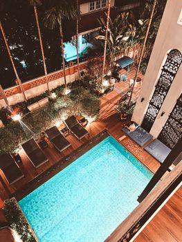 Aerial view of a luxurious outdoor pool surrounded by lounge chairs and lush greenery, creating a serene night atmosphere.