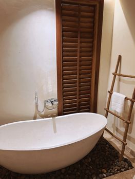 Minimalist bathroom featuring a stone-laden freestanding tub and wooden shutters.