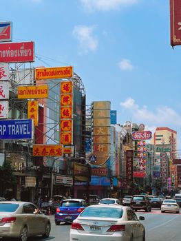 View of a busy street in Chinatown, Bangkok with vibrant signs and traffic under a clear sky.