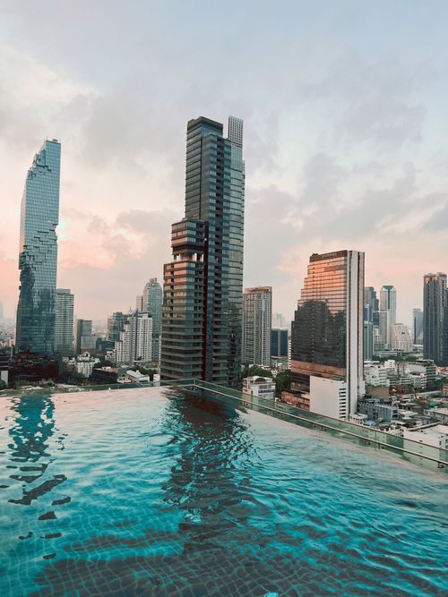 Free Breathtaking view of Bangkok skyline reflecting in a stylish rooftop pool at sunset. Stock Photo