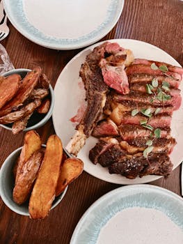 Sliced ribeye steak and roasted potatoes on a wooden table, ready to serve.