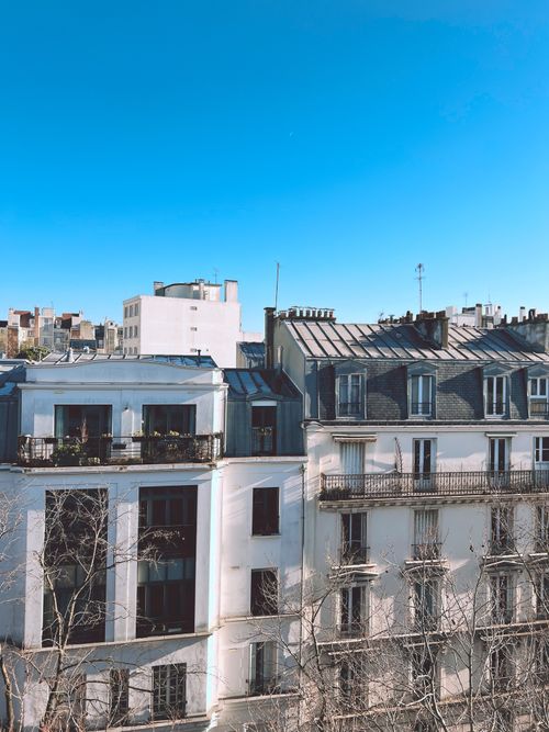 Free Charming view of Parisian rooftops captured under a vibrant blue sky, showcasing classic architectural elegance. Stock Photo