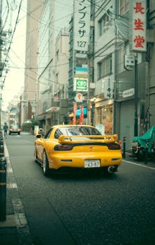 A vibrant yellow sports car drives through Shinagawa City, Tokyo, Japan, capturing urban street life.