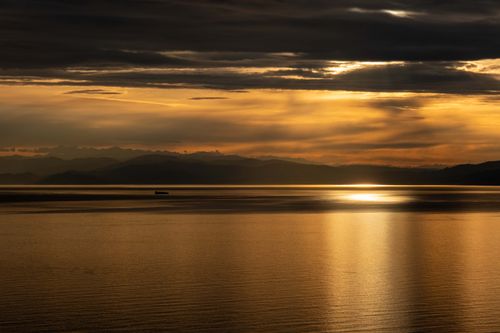 Free Stunning sunset view with golden hues over a calm sea and distant mountains. Stock Photo