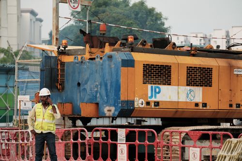 Free Worker on phone at construction site with large machinery in urban setting. Stock Photo