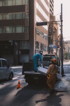 City workers loading materials onto a truck on a sunny urban street corner.