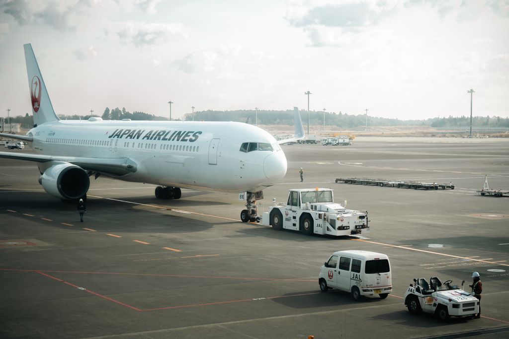 Japan Airlines aircraft stationed on the tarmac in Tokyo with ground crew vehicles.