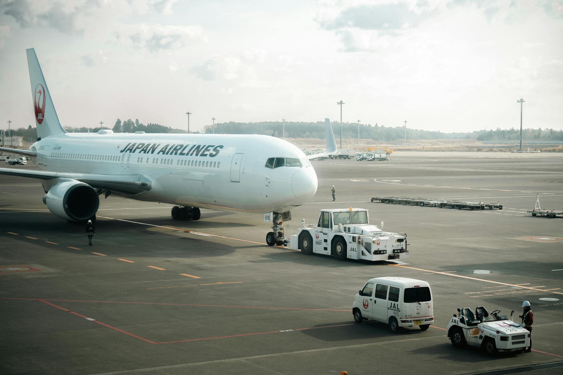 Japan Airlines aircraft stationed on the tarmac in Tokyo with ground crew vehicles.