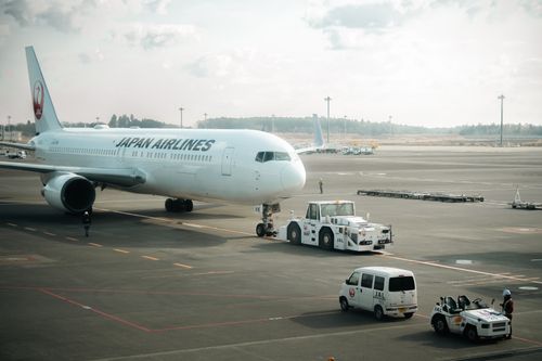 Free Japan Airlines aircraft stationed on the tarmac in Tokyo with ground crew vehicles. Stock Photo