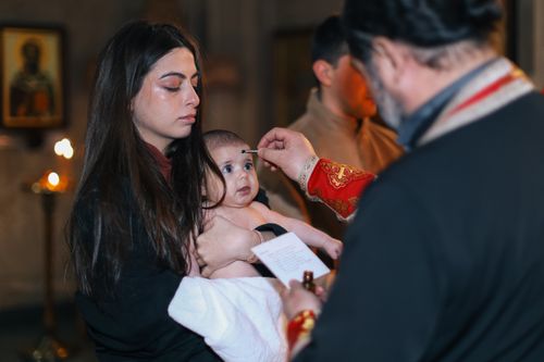 Free A solemn baptism ceremony with a baby and family inside a church, highlighting spiritual traditions. Stock Photo