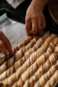 Close-up of hands arranging twisted pastry dough sticks on a baking tray.