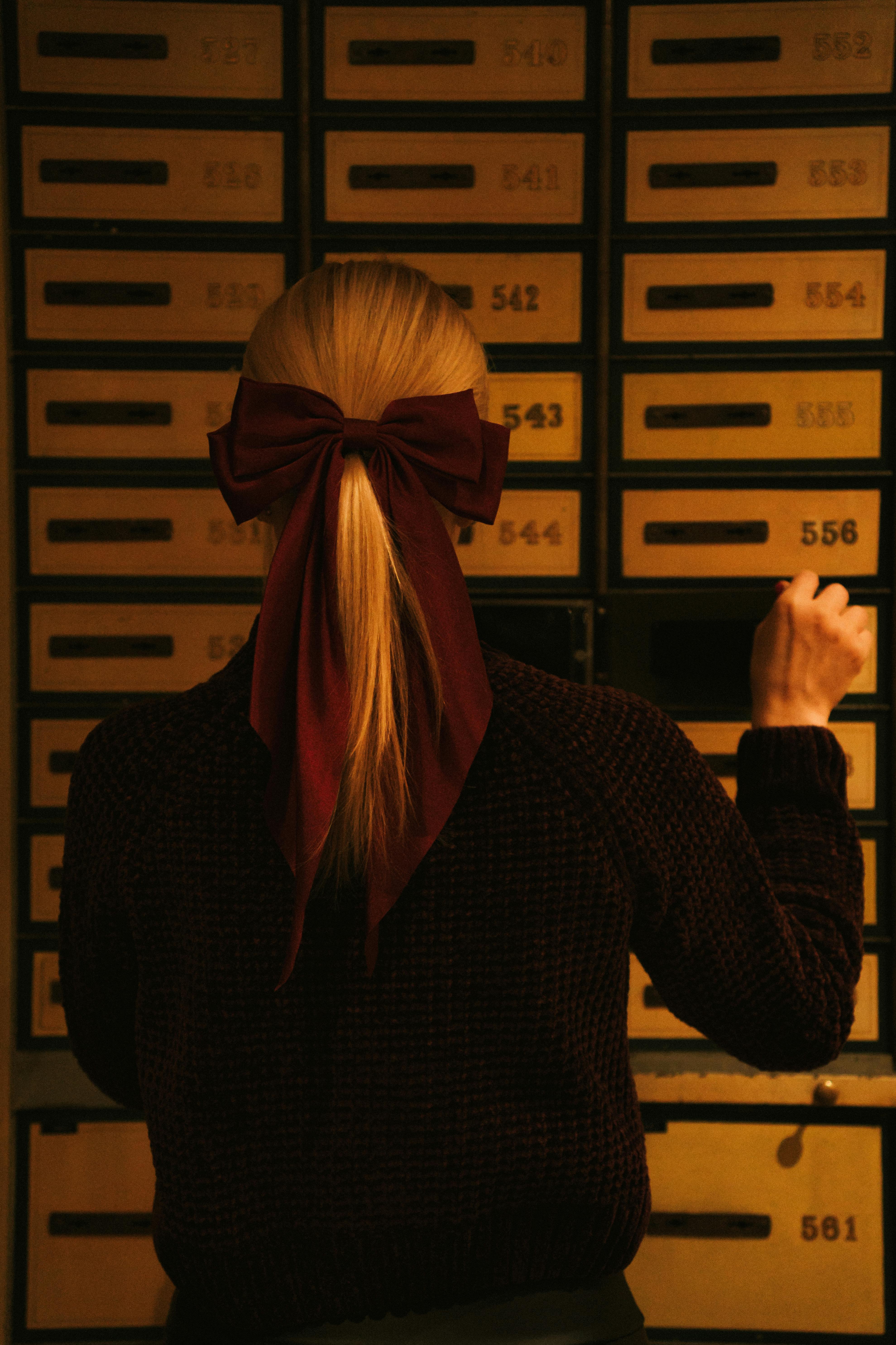 Back view of a woman wearing a burgundy bow facing numbered lockers in moody lighting.
