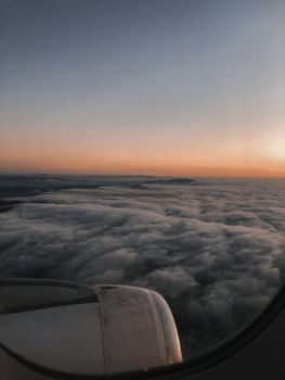 View from airplane window showcasing clouds below and vivid sunrise colors.