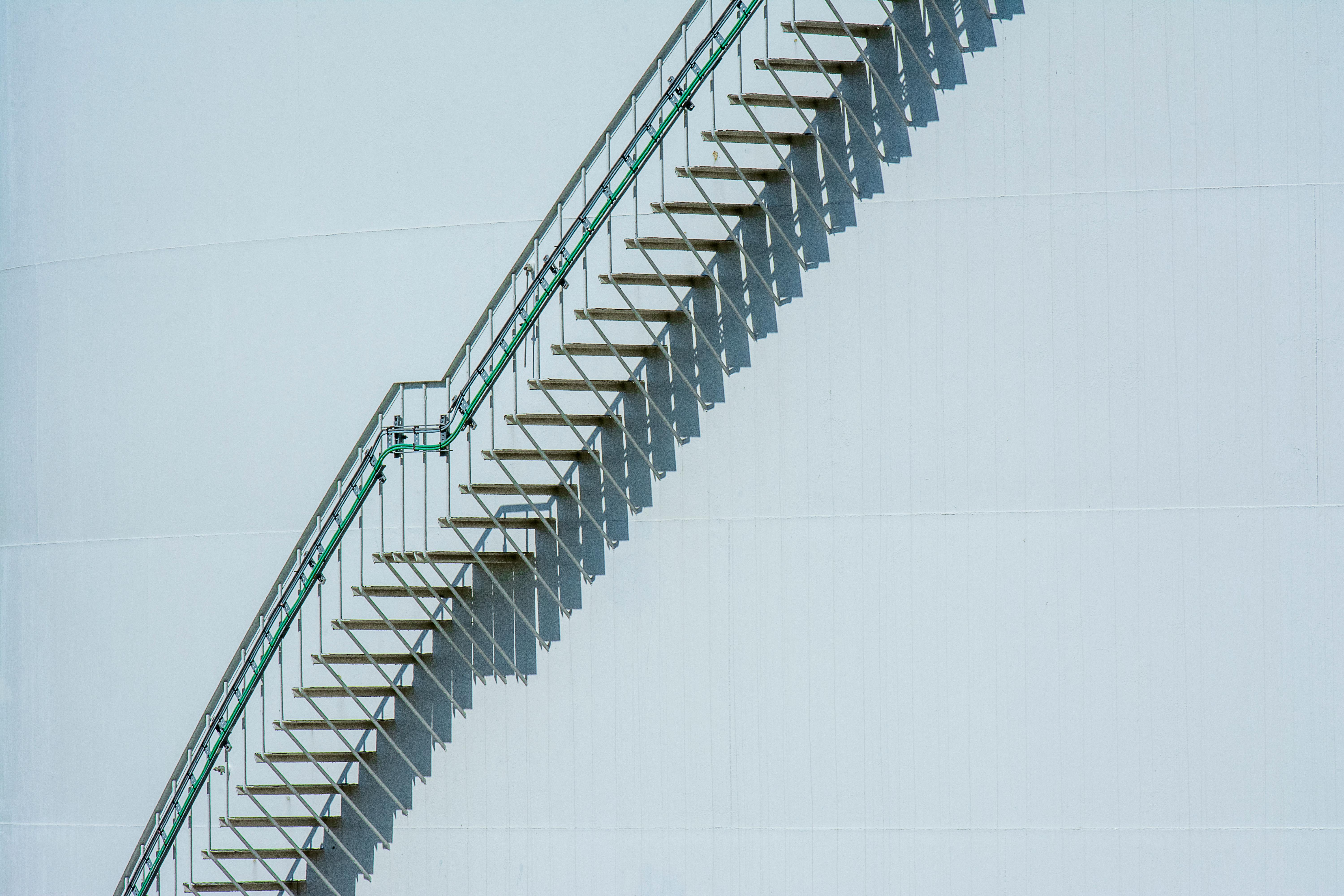Free Diagonal metal stairs casting shadows on a white industrial building facade. Stock Photo