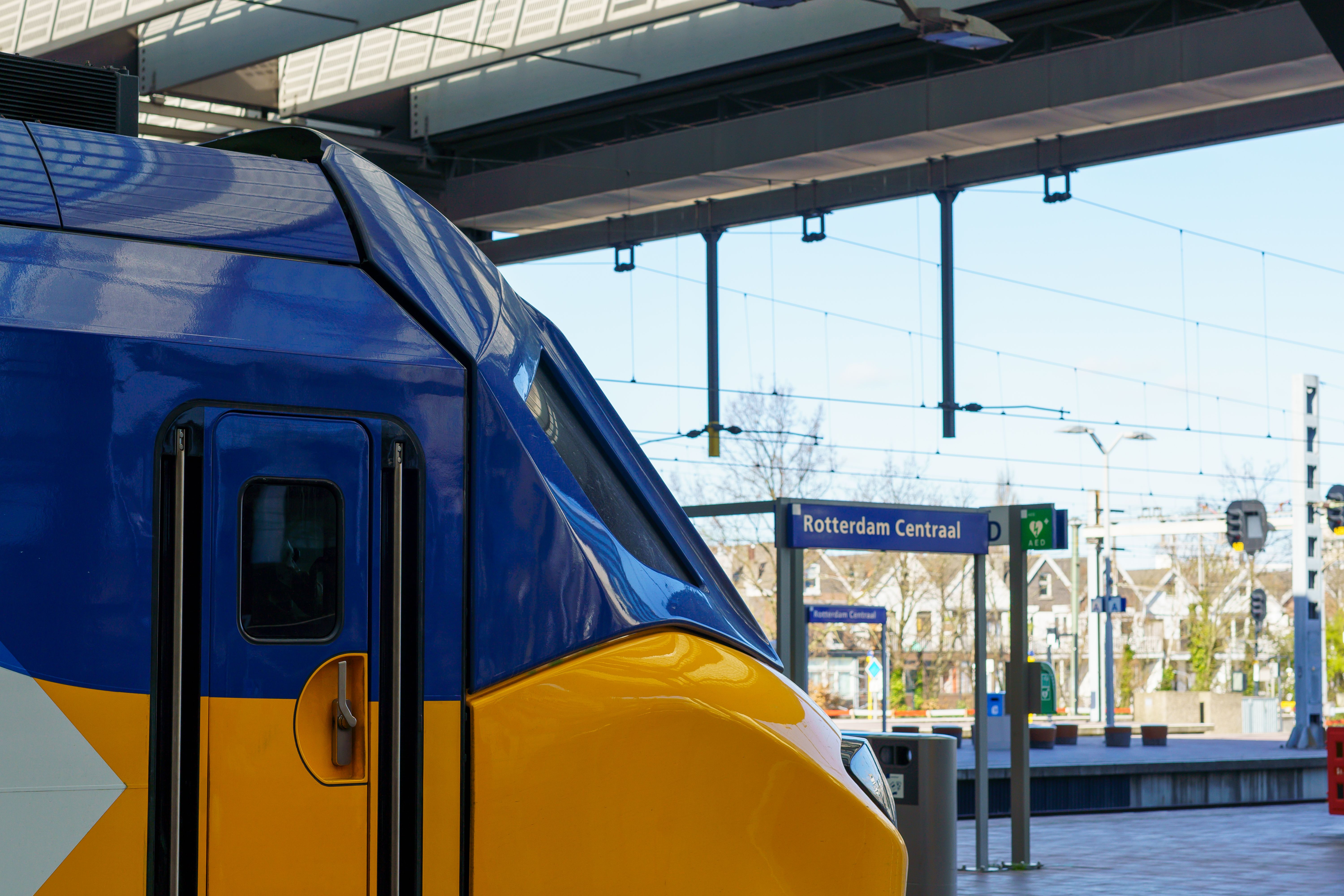 Train stands at Rotterdam Central station platform beside a station sign under a covered roof