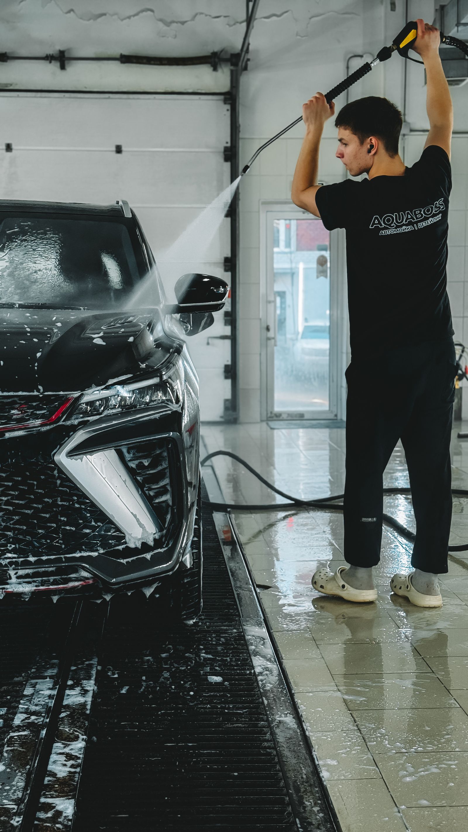 A dark car covered in cleaning foam being washed at the bay