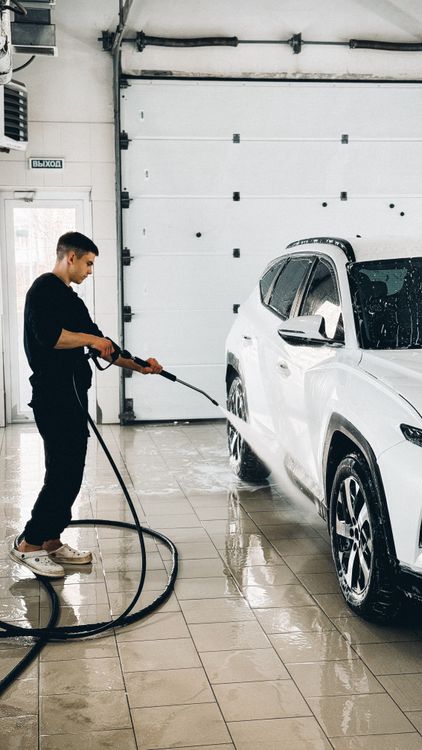 A man power washing a car in a garage.