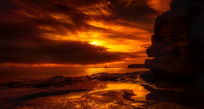 A stunning sunset over the sea with silhouetted cliffs, creating a vivid orange sky.