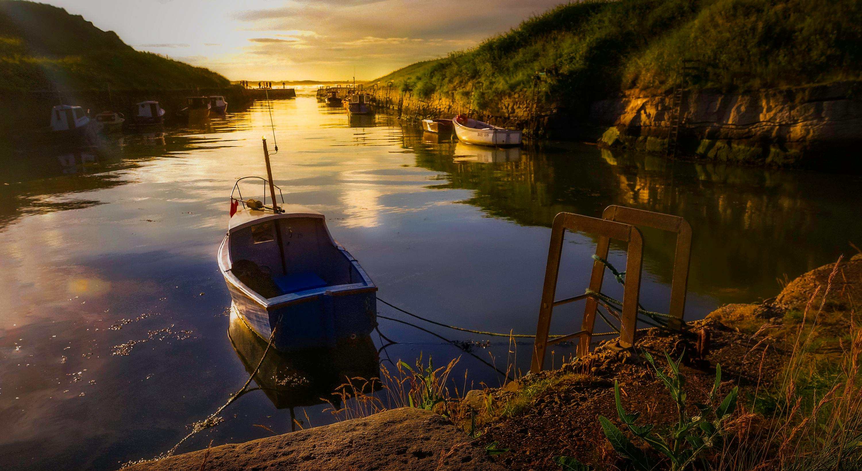 日落时分，一艘孤舟静静漂浮在平静的海湾，倒影映在水面上