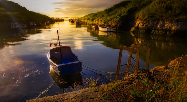 日落时分，一艘孤舟静静漂浮在平静的海湾，倒影映在水面上