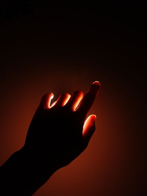 Free Silhouette of a hand against a glowing light background, creating a warm and dramatic effect. Stock Photo