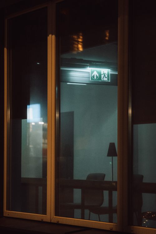Free View through a window of an office interior at night with an illuminated exit sign. Stock Photo