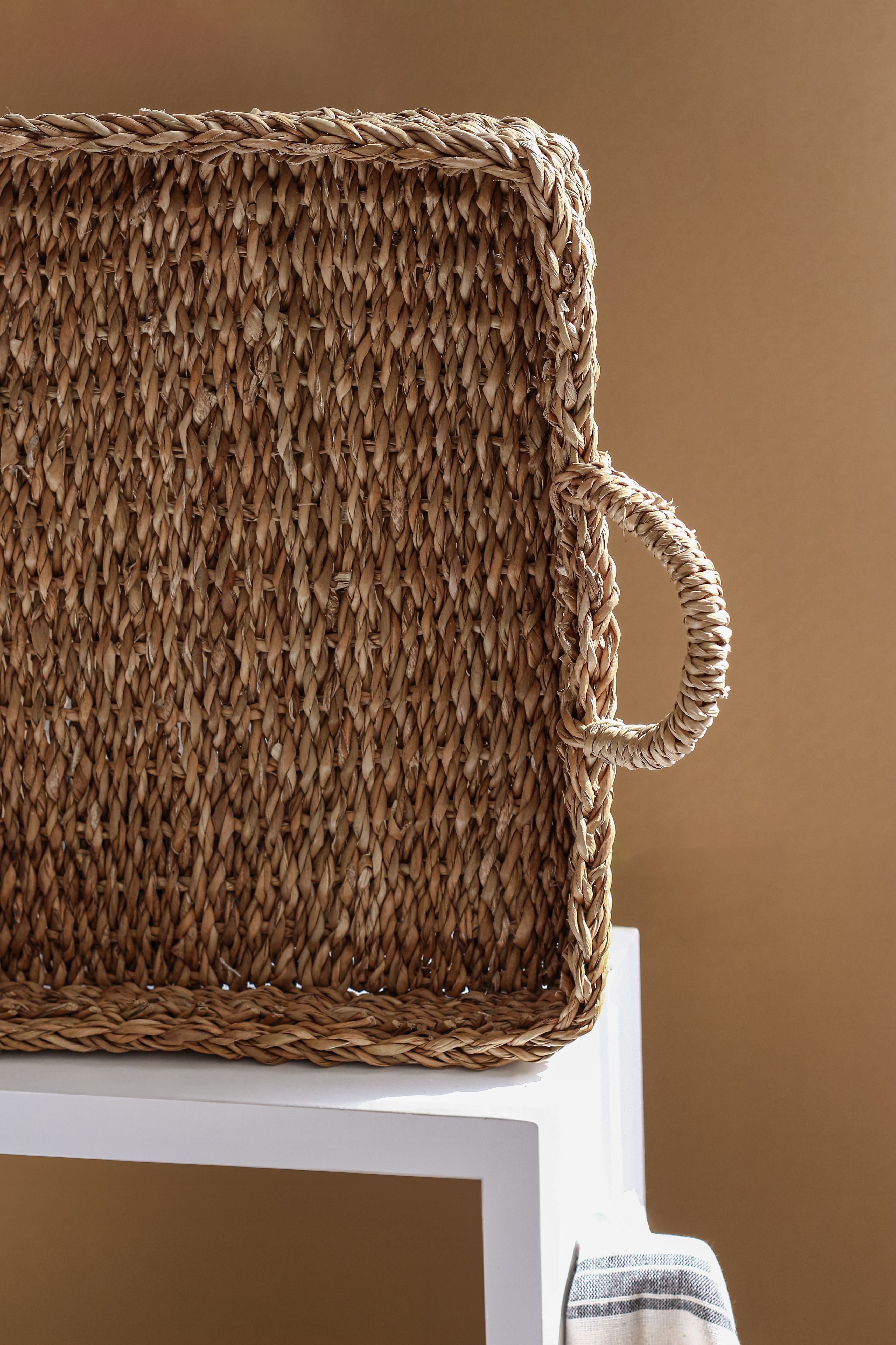 Elegant woven basket with handles resting on a modern white stand against a neutral background.