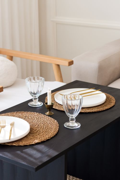 Free Minimalist table setup featuring woven placemats, glassware, and a candle for an intimate indoor dining experience. Stock Photo