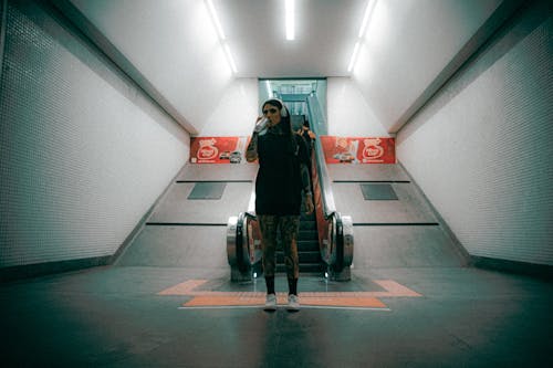 Free Young woman with headphones and tattoos drinking water on subway escalator. Urban lifestyle concept. Stock Photo