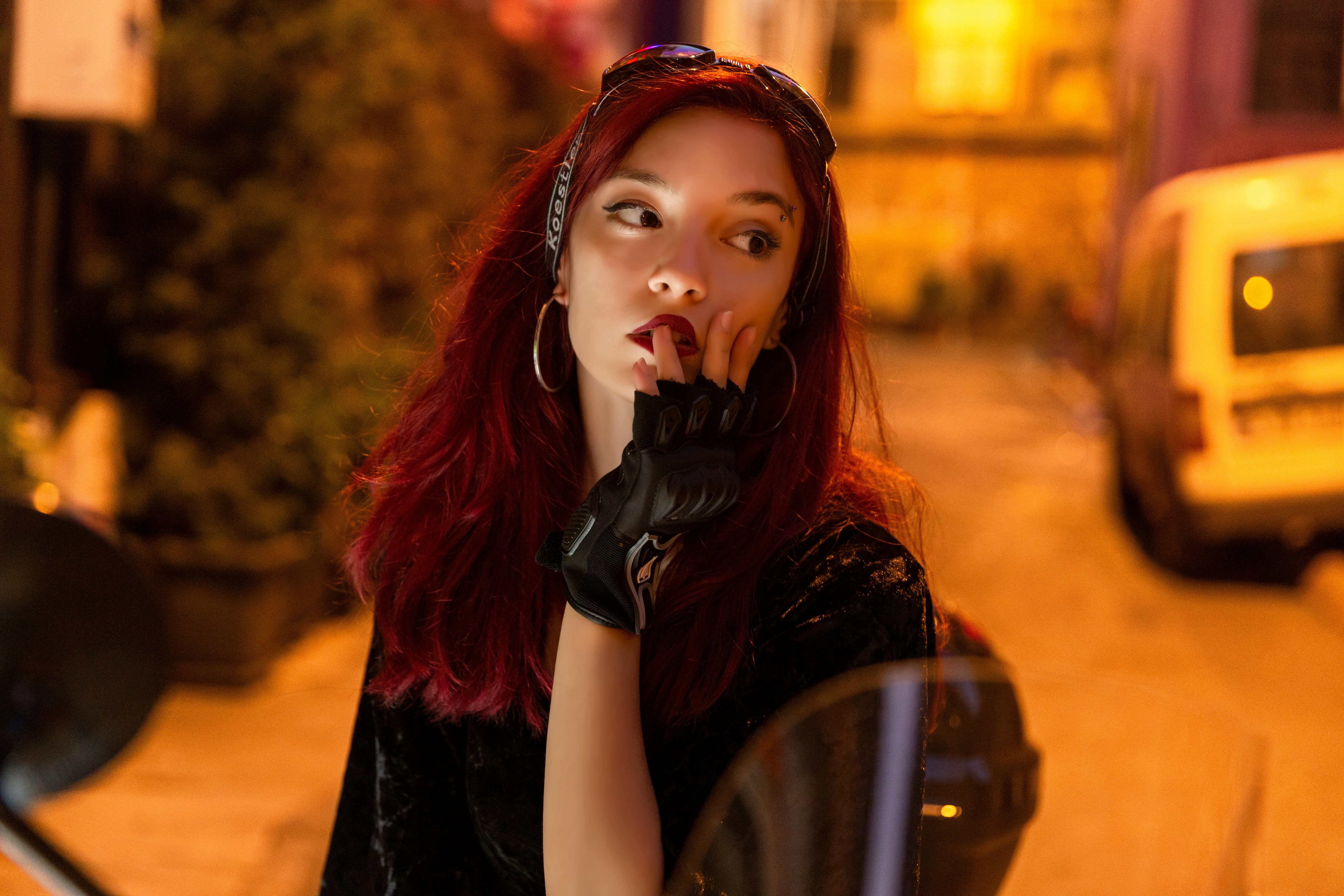 De franc Retrat d'una dona amb els cabells vermells i els guants posant a l'aire lliure a la nit, emanant moda urbana. Foto d'estoc