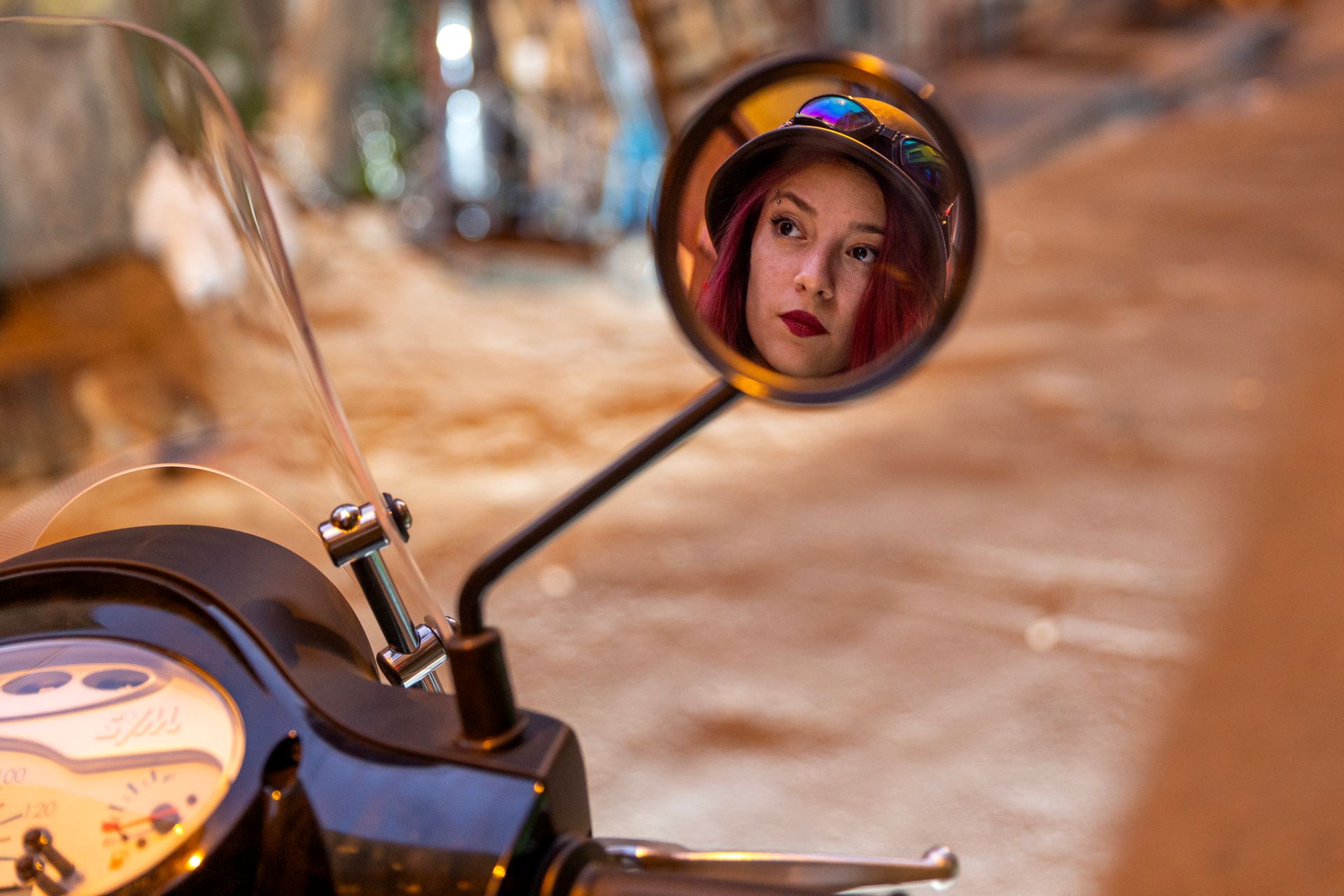 A stylish woman with red hair reflected in a classic motorcycle mirror.