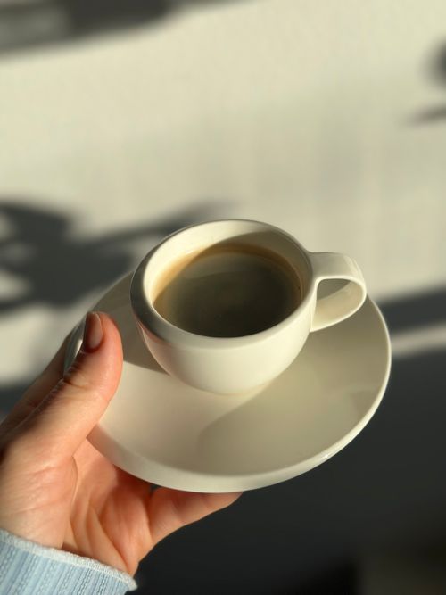 Free A close-up of a hand holding a cup of coffee with sunlight casting shadows. Stock Photo