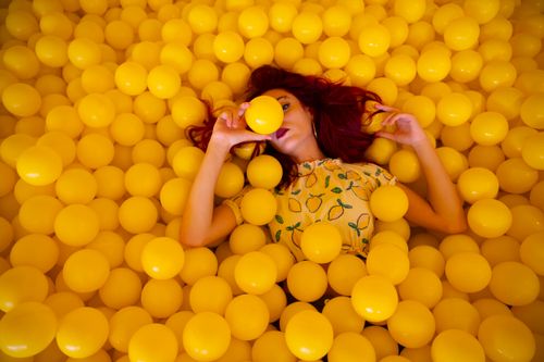 Free Woman with red hair in a yellow ball pit, creating a colorful and playful portrait. Stock Photo